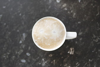 Overhead view of frothy cappuccino in white cup on dark marble