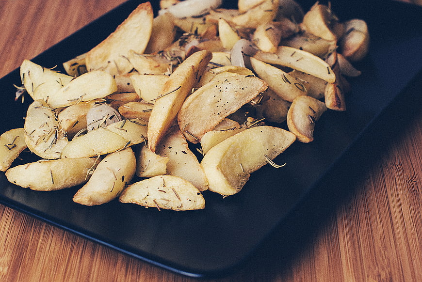Roasted potato wedges with rosemary on black plate