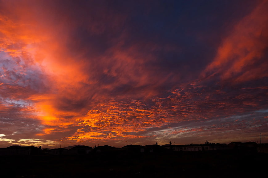 Dramatic fiery orange sunset sky over dark suburban silhouette