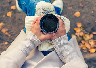 First-person view of hands holding a black coffee cup in autumn
