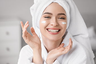 Happy woman with towel on head applying face cream