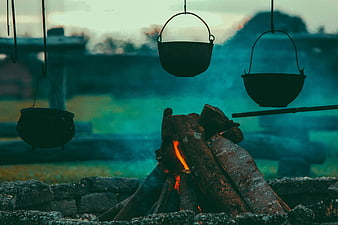 Cast iron pots hanging over a rustic campfire with smoke