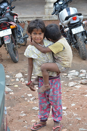 Young Indian boy carrying younger sibling on dusty street