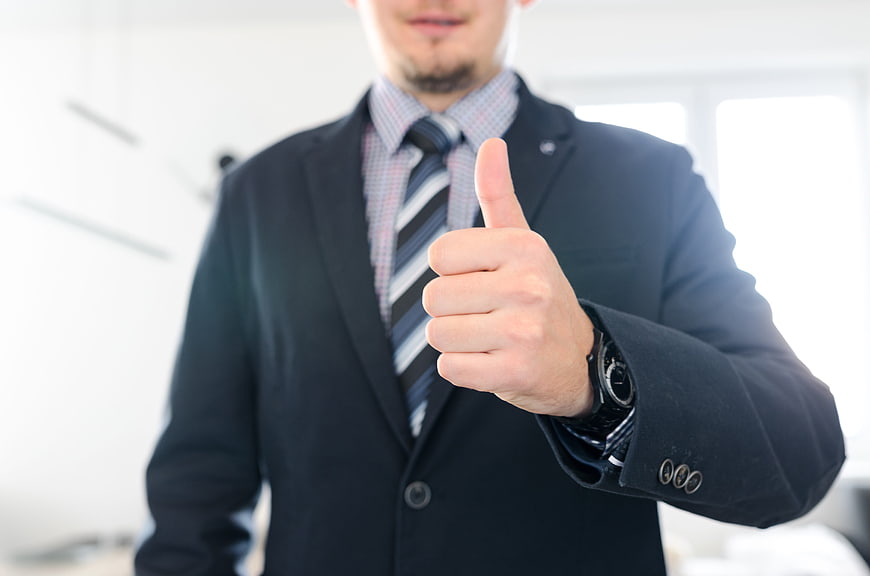 Businessman in dark suit giving thumbs up in bright office