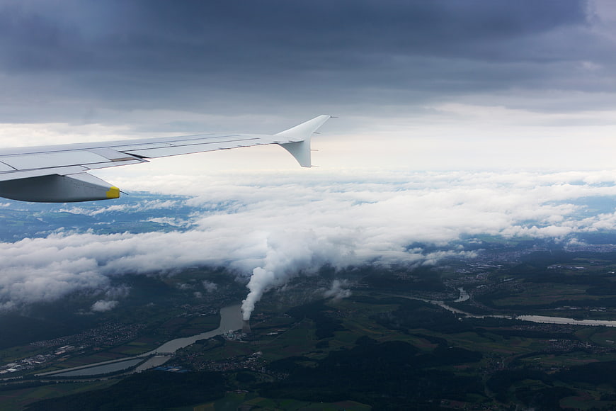 Airplane Wing Over Cloudy Landscape with Smokestack