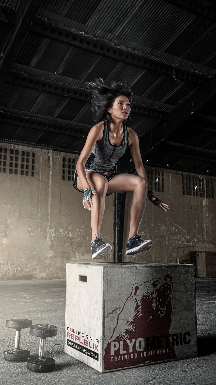 Athletic woman jumping onto plyometric box in gym