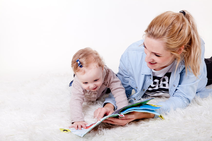 Mother and baby reading book on white rug
