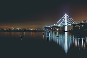 Illuminated suspension bridge at night with water reflections