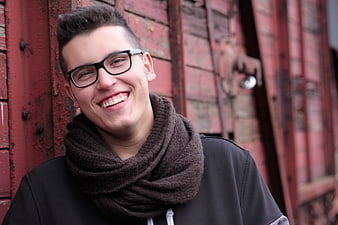 Happy young man with glasses and scarf smiling outdoors