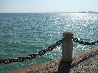 Rusty Chain Fence Along Sparkling Sea Coastline