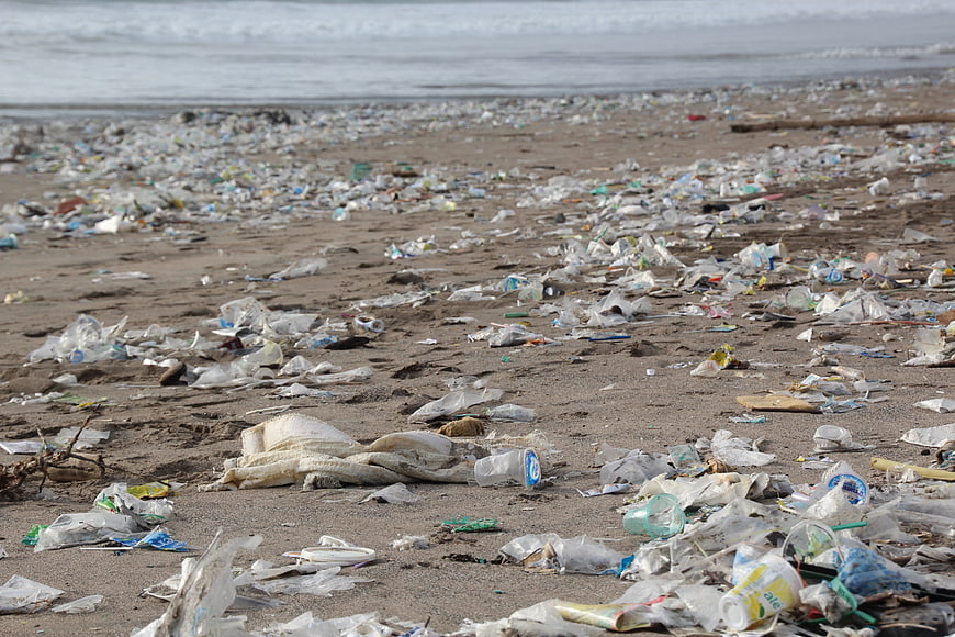 Plastic waste and garbage scattered across a polluted sandy beach shoreline