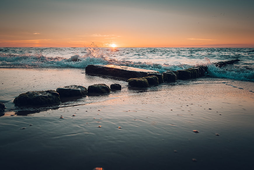 Sunset over ocean waves crashing on rocky beach