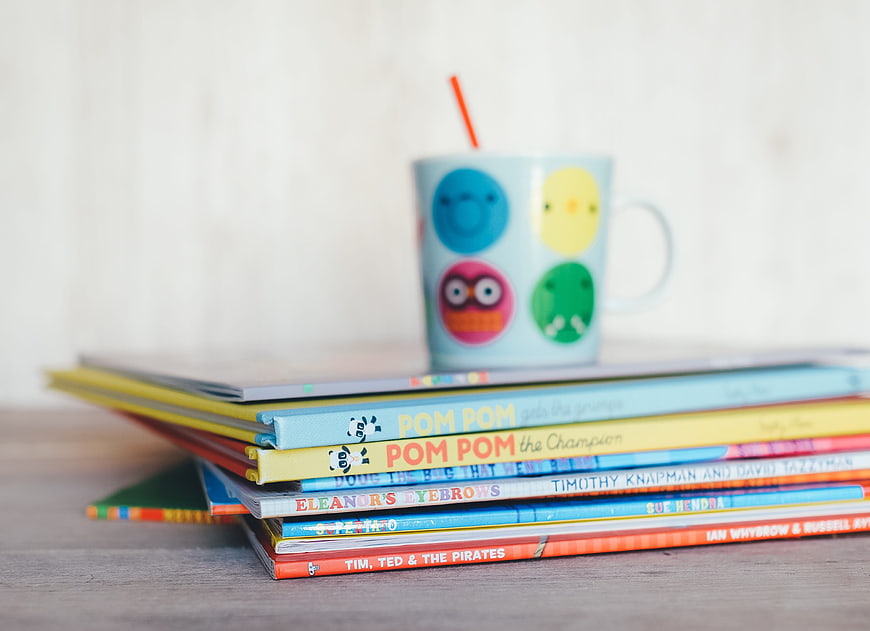 Stack of colorful children's books with a mug
