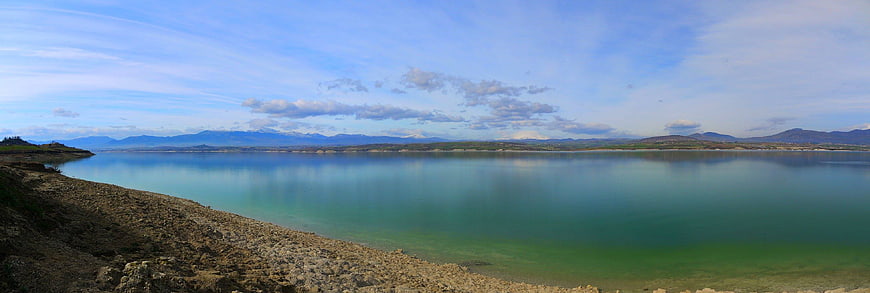 Panoramic view of calm turquoise lake with rocky shore and mountains