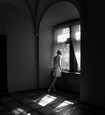 Woman in white dress looking out window in black and white