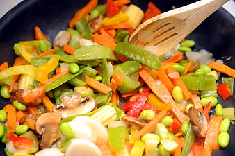 Colorful stir-fried mixed vegetables in a black wok with wooden spatula