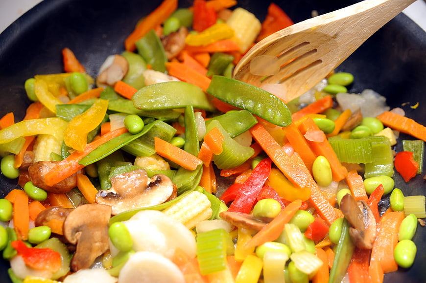 Colorful stir-fried mixed vegetables in a black wok with wooden spatula