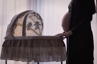 Pregnant woman standing beside a baby bassinet with mobile