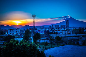 Sunset over cityscape with smoking volcano and cell tower
