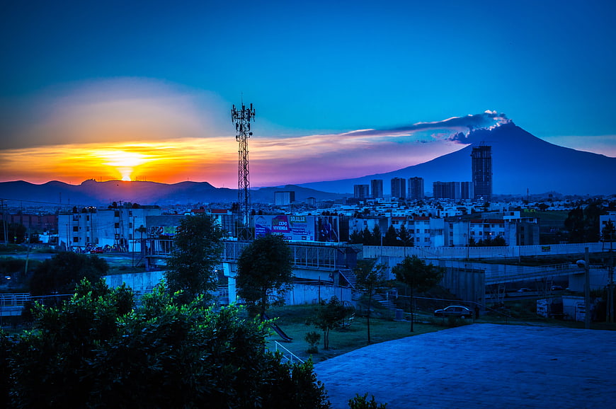 Sunset over cityscape with smoking volcano and cell tower