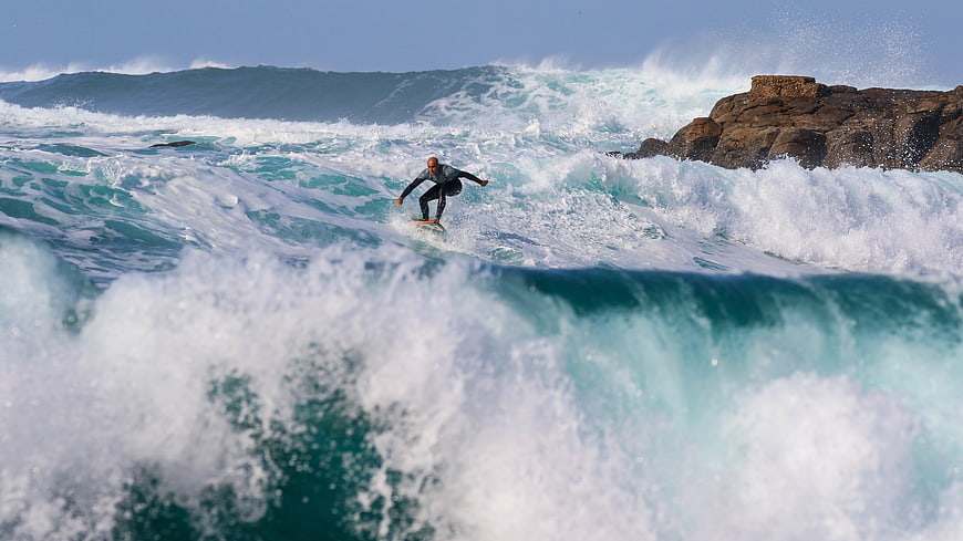 Surfer Riding Powerful Ocean Wave Near Rocky Coastline