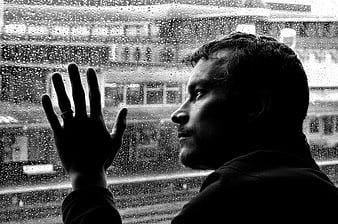 Black and white portrait of a man looking out a rainy window