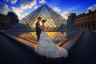 Wedding couple embracing in front of Louvre Pyramid at sunset