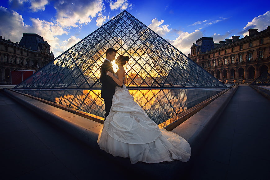Wedding couple embracing in front of Louvre Pyramid at sunset
