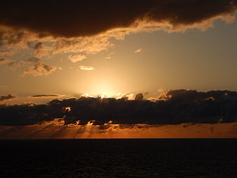 Dramatic sunset over ocean with sun rays through clouds