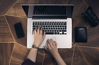 Top view of hands typing on laptop with camera lens and smartphone