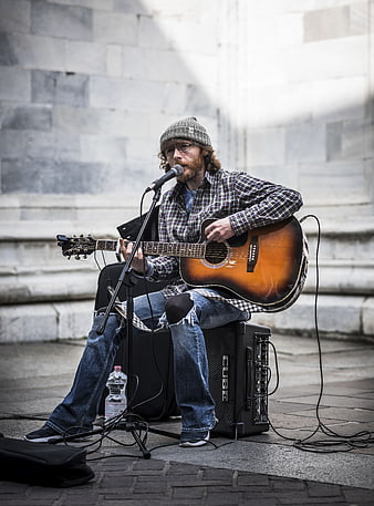 Street musician playing acoustic guitar and singing into microphone