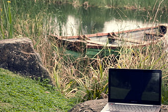 Laptop on rock by lake with boat in background