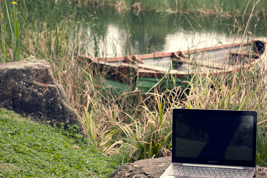 Laptop on rock by lake with boat in background