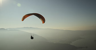 Paraglider soaring over misty mountains at sunrise