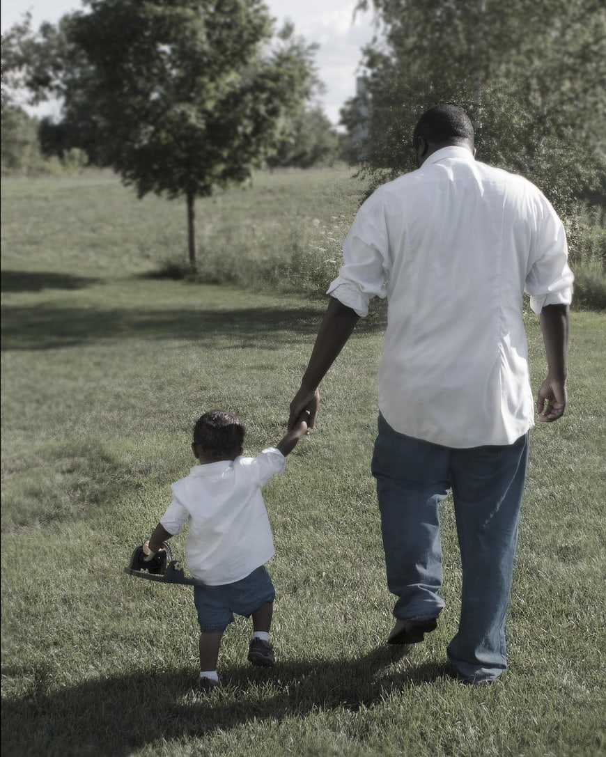 Father and young son holding hands walking through a grassy field