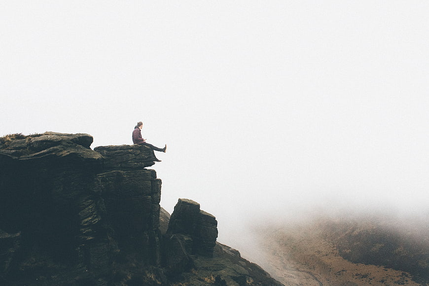 Man sitting on rocky cliff edge in thick fog