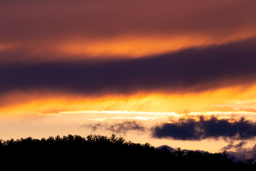 Dramatic sunset with orange clouds over dark forest silhouette