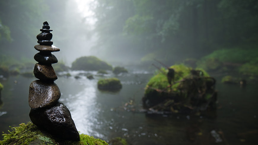 Stacked stones in misty forest stream