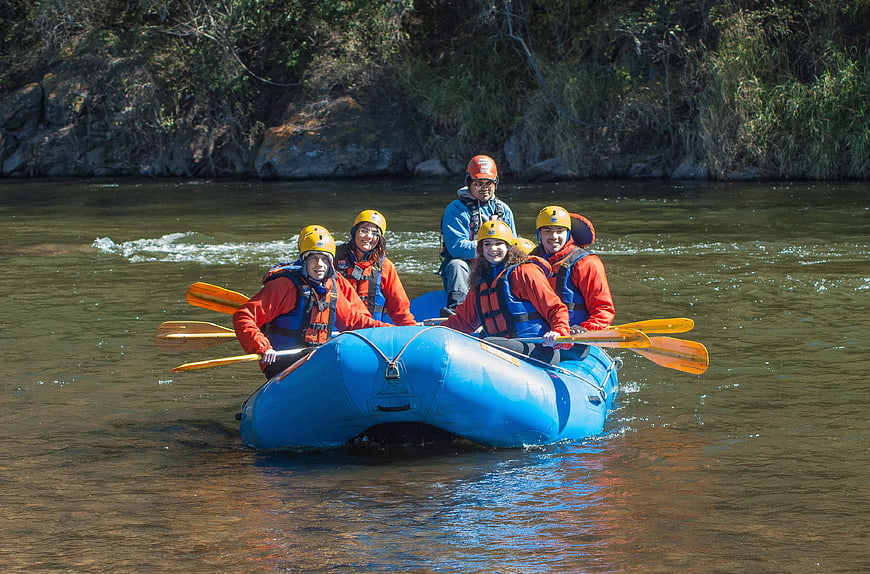 Group of people paddling a blue inflatable raft on a river