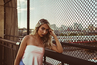 Stylish blonde woman posing by chainlink fence in urban setting