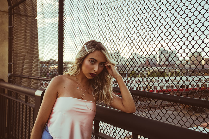 Stylish blonde woman posing by chainlink fence in urban setting