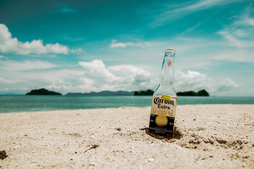 Empty Corona Extra beer bottle on tropical sandy beach