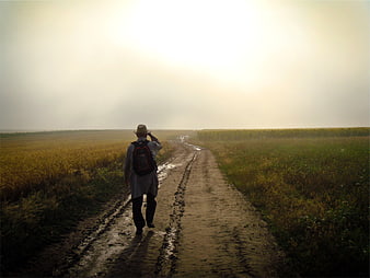 Man with backpack walking on muddy rural road at dusk
