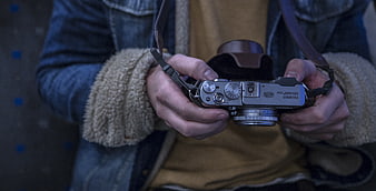 Close-up of hands holding silver Fujifilm X100 camera
