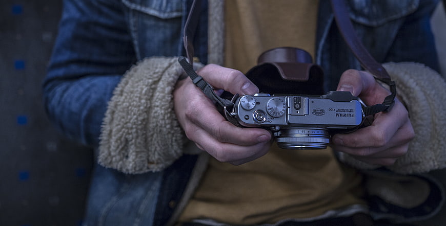 Close-up of hands holding silver Fujifilm X100 camera