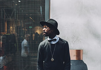 Stylish man in fedora and bowtie standing by window