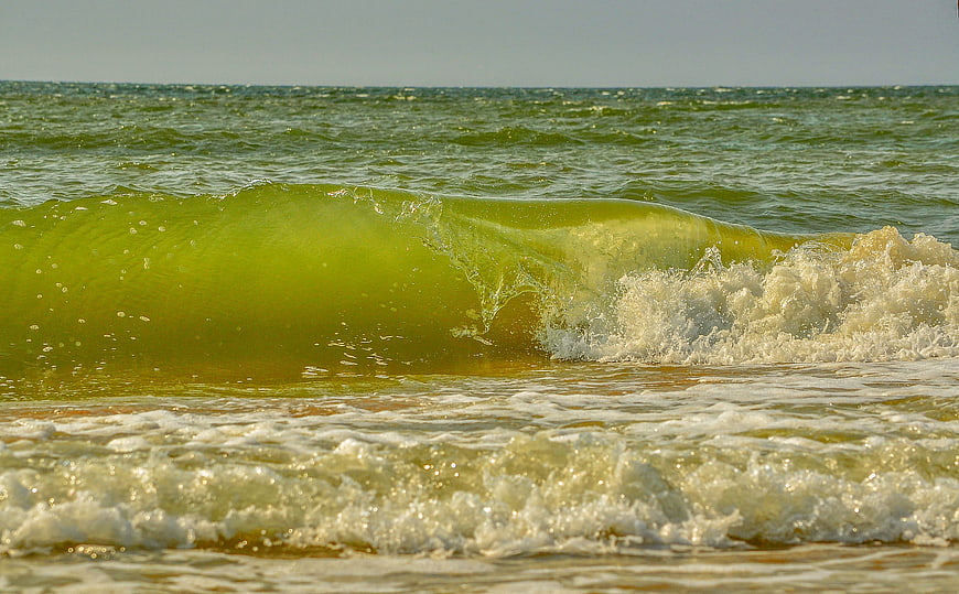 Close-up of a translucent green ocean wave breaking with foam