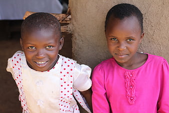 Two African girls smiling outdoors against a textured mud wall