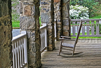 Rustic wooden rocking chair on stone porch with garden view