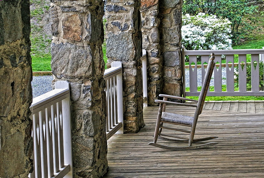 Rustic wooden rocking chair on stone porch with garden view